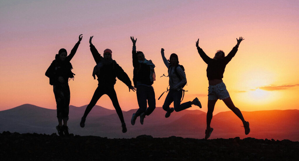 five teens jumping in a sunset